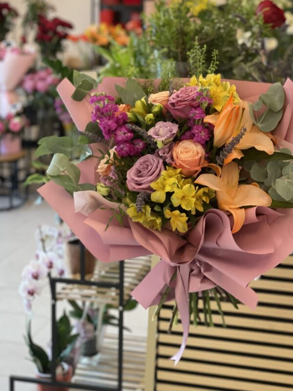 Buchet premium cu trandafiri lila, crini somon, alstroemeria galbenă și mathiola mov, realizat în florăria Fir de Rai Brașov.