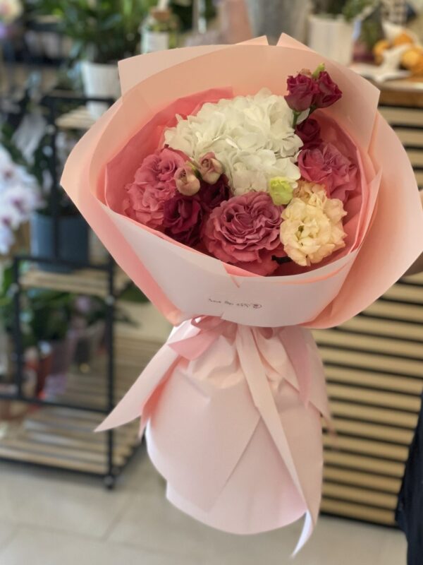Buchet floral premium cu hortensie albă, trandafiri roz vintage și lisianthus, ambalat elegant în hârtie roz pastel.
