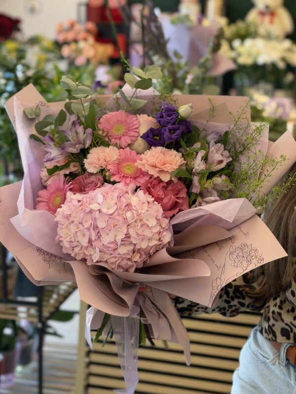 Buchet floral premium cu hortensie roz, trandafiri, gerbera și lisianthus mov, ambalat elegant în hârtie pastel.