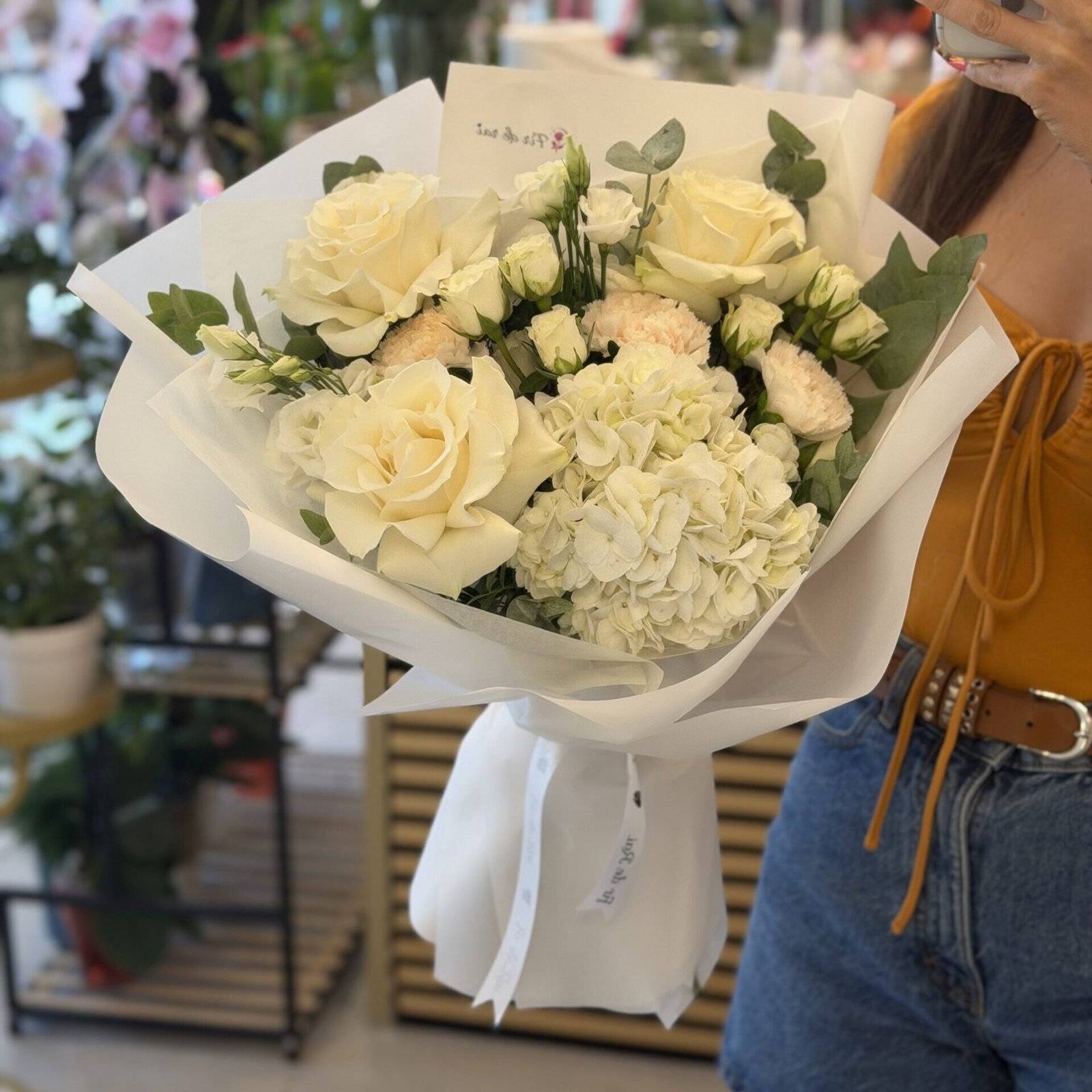 Buchet premium alb cu hortensie, trandafiri ivoire, miniroze și garoafe crem, ambalat elegant în hârtie albă.
